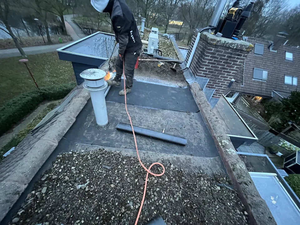 Nieuwe toplaag bitumen wordt gebrand op een plat dak