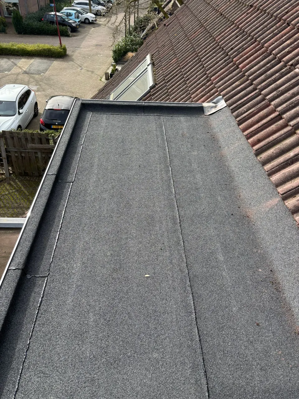 Grootschalige bitumen dakrenovatie in uitvoering, nieuw dakvlak naast een pannendak